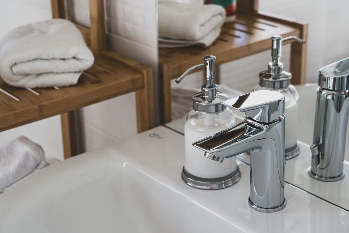 Chrome faucet and matching bathroom dispensers beside a basin